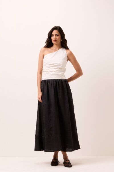 Saia midi preta em rami, corte rodado evasê, cintura alta e barra ampla, usada com blusa off-white de um ombro só em estúdio