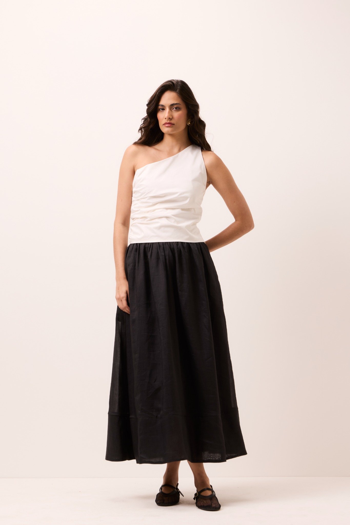 Saia midi preta em rami, corte rodado evasê, cintura alta e barra ampla, usada com blusa off-white de um ombro só em estúdio