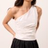 Blusa off-white de um ombro só com drapeado lateral e frente dupla, vestida pela modelo