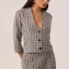 Modelo vestindo blusa vichy preto e branco de algodão, mangas 7/8 e decote V com botões, usada aberta como casaqueto