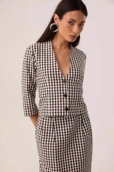 Modelo vestindo blusa vichy preto e branco de algodão, mangas 7/8 e decote V com botões, usada aberta como casaqueto