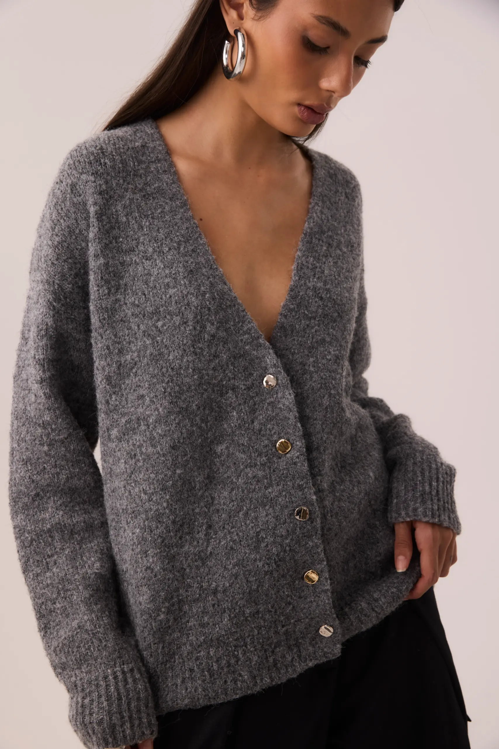 Cardigan oversized cinza em tricot com lã, decote V, botões de metal dourado e prata, mangas longas com punhos largos, comprimento abaixo do quadril